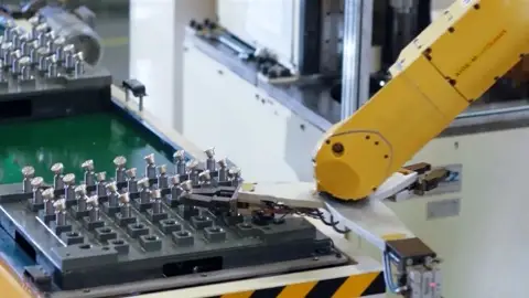 Yellow robot arm handling rows of small hydraulic valve components on a production fixture