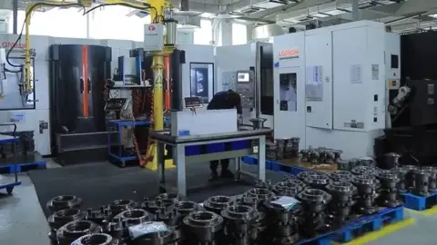 Machining hall with CNC machines and stacks of flanged component housings in the foreground